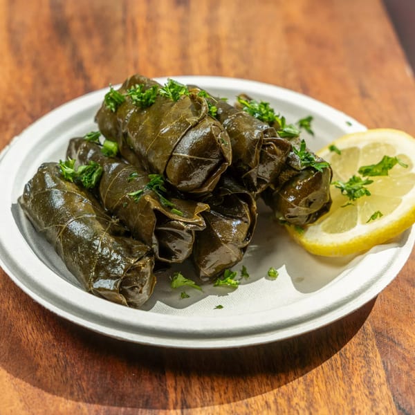 Hovan Gourmet Mediterranean dolmas, grape leaves stuffed with rice and herbs, garnished with parsley and lemon.