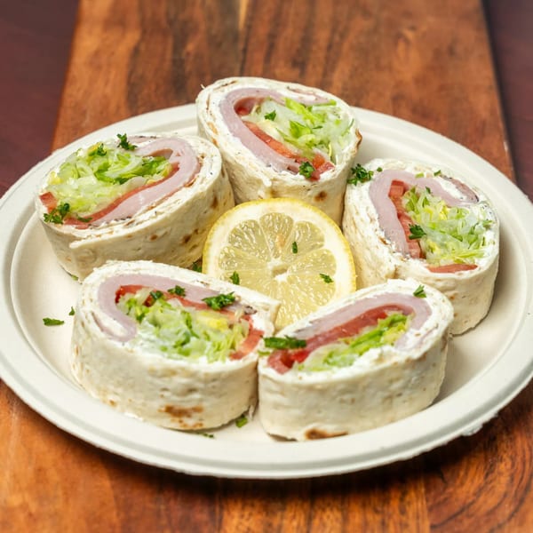 Five Hovan Gourmet Mediterranean turkey and cheese pinwheel wraps with lettuce, tomato, and a lemon slice.