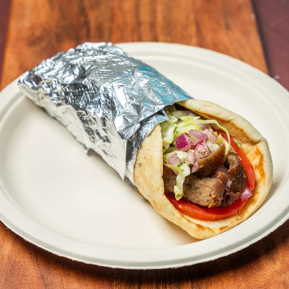 Hovan Gourmet Mediterranean gyro wrap with meat, lettuce, tomatoes, and onions, partially wrapped in foil.