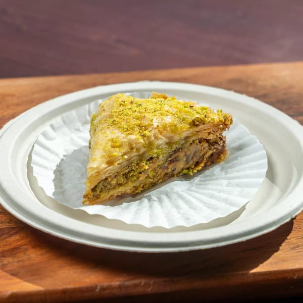A triangular slice of Hovan Gourmet baklava, topped with crushed pistachios, on a white plate.