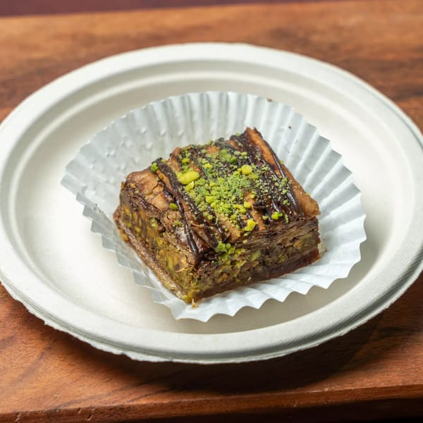 Hovan Gourmet Mediterranean baklava with chocolate drizzle and pistachio crumbles on a white plate.